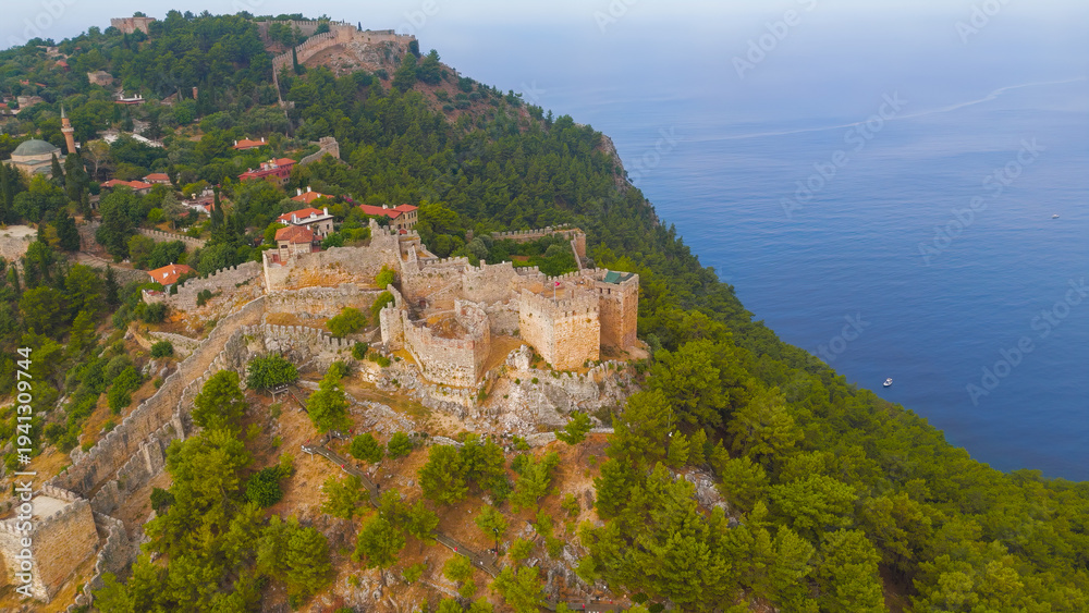 Fototapeta premium Alanya, Turkey. Ehmedek Castle emerging from green forest on mountainside, aerial drone view in summer morning.. Aerial View