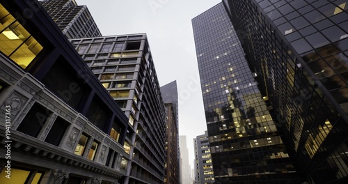 massing of vintage masonry building beside glossy black tower, surveyor perspective capturing architectural contrast, lit office windows, narrow street vista,