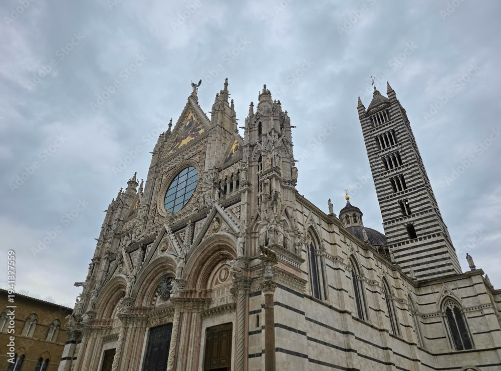 Fototapeta premium Facade and Bell Tower of Siena Cathedral (Duomo di Siena), Italy. Ornate Gothic Architecture with Marble Stripes and Rose Window under Cloudy Sky in Tuscany. Historic Italian Landmark