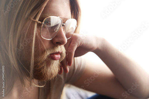 Portrait of pensive young man with long blond hair wearing spectacles