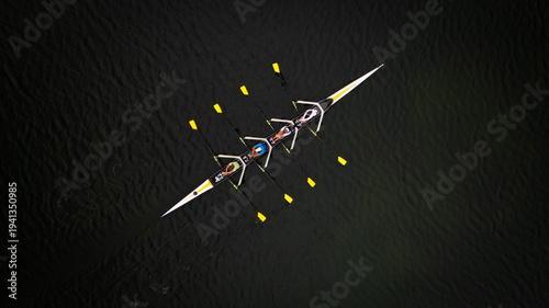 Aerial view of a sleek rowing boat cuts through the dark, still waters, its bright yellow oars a stark contrast to the shadowy depths, Divonne-les-Bains, Auvergne-Rhone-Alpes, France.