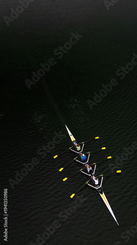 Aerial view of a sleek rowing boat slicing through the dark, reflective waters, its oars creating golden splashes, Divonne-les-Bains, Auvergne-Rhone-Alpes, France.