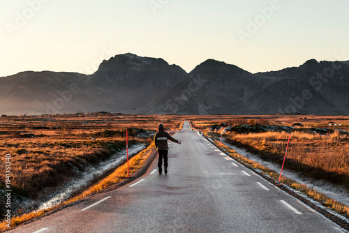 Norway, Lofoten Islands, back view of man hitchhiking at empty country road
