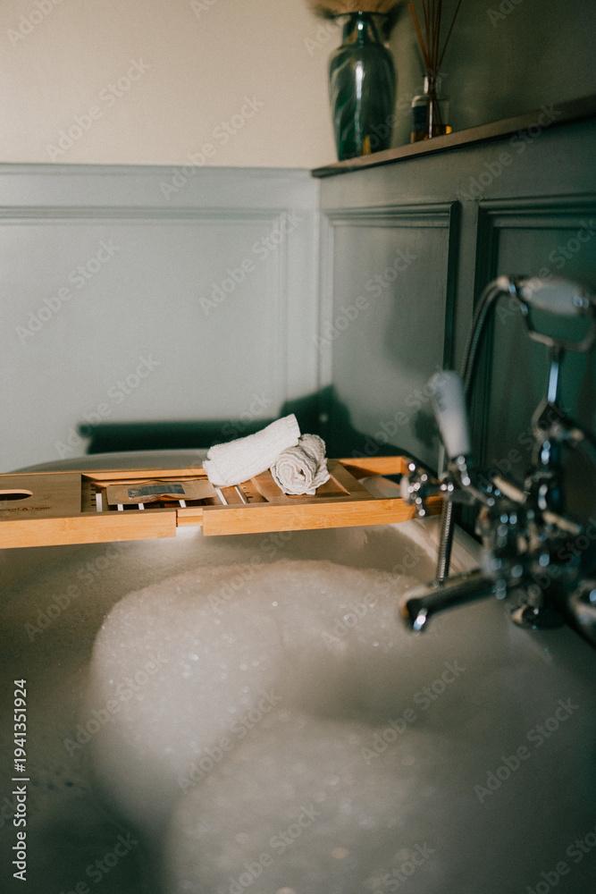 Φωτογραφία Bubbly bathtub with wooden tray holding rolled towels and bath items