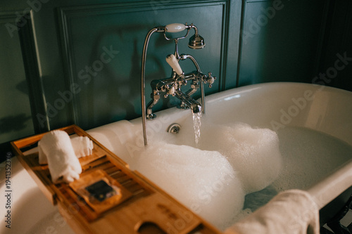 Fotografie Luxurious clawfoot bathtub filled with bubbly water, set against dark teal walls