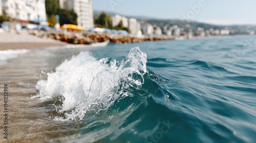 A close-up view of a gentle wave crashing onto a serene beach, showcasing the clear blue water and distant coastal buildings, inviting relaxation and peace.
