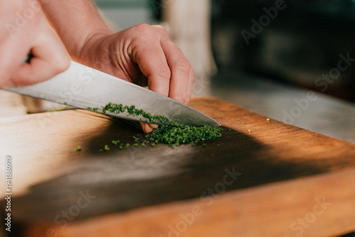 Schilderij op canvas Person finely mincing fresh green herbs with a knife on a wooden board