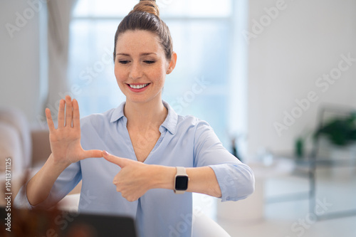 Smiling cute young woman explaining something on video call by sign language