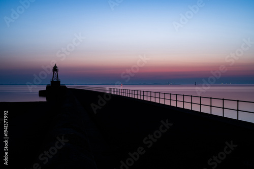 Old Mole on the horizon at dawn with a tranquil atmosphere and pink-blue sky, view of the North Sea or Jade Bay in the morning near the cross-range light, Old Mole in 26382 Wilhelmshaven, Germany