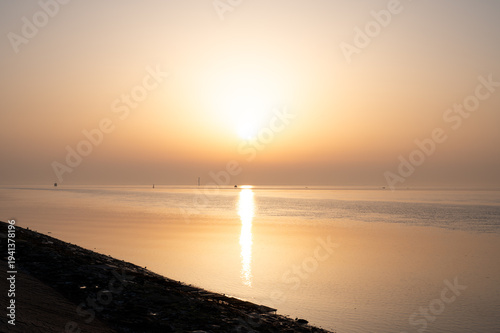 The sunrise reflects golden light on the calm sea, creating a peaceful morning atmosphere; view of the North Sea or Jade Bay in the morning at the former second entrance in 26382 Wilhelmshaven, German