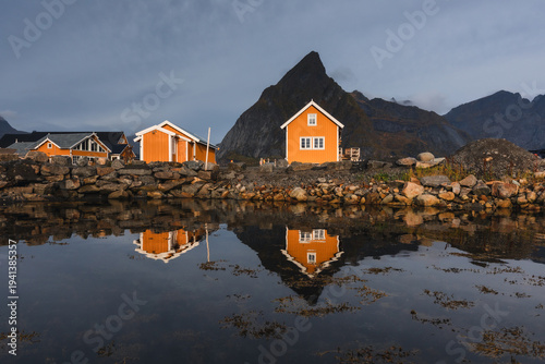 Stunning fall scenery in the Lofoten Islands. Iconic red rorbu cabins nestled between rocky coastlines and dark arctic waters during the golden hour. Travel Norway.
