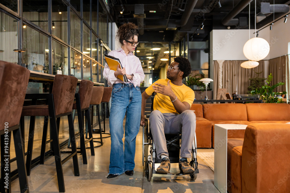 Obraz premium Businesswoman holding folders discussing with disabled man in shared workspace