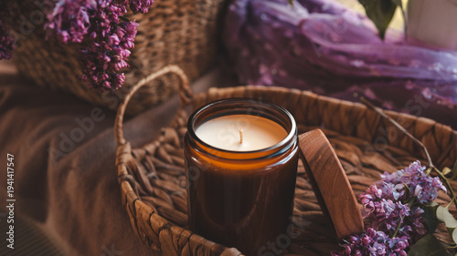 Fotografie Aesthetic candle with lilac flowers and woven basket, cozy home decor concept