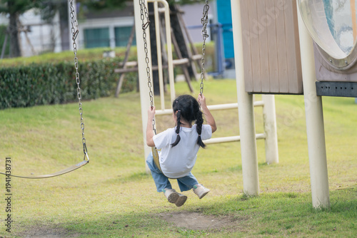 Joyful Child Swinging on Playground Swing in Sunny Park, Enjoying Outdoor Fun and Freedom in Simple White T-shirt and Blue Jeans