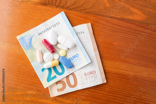 Some pills and euro banknotes on a wooden table.
