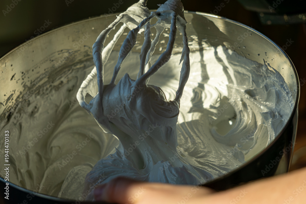 Fototapeta premium Whipped meringue mixture on mixer whisk in metal bowl