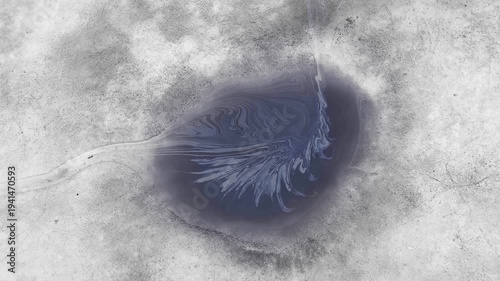 Motor oil forming iridescent pattern in melting snow puddle illustrating environmental pollution.