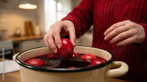 Woman dyeing red Easter eggs in a kitchen pot, spring family tradition, holiday preparation, festive process, Easter celebration.