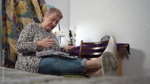 Senior elderly woman is engaged in needlework, talking and arranging scraps. Hand sewing.