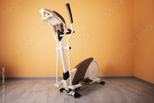 Sleek elliptical exercise machine in a minimal home interior with orange wall and marble floor, perfect for fitness and healthy lifestyle concepts.