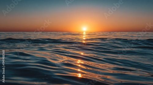 Golden sunset over calm ocean horizon with glowing reflections on gentle waves, peaceful coastal landscape capturing warm evening light and serene atmosphere