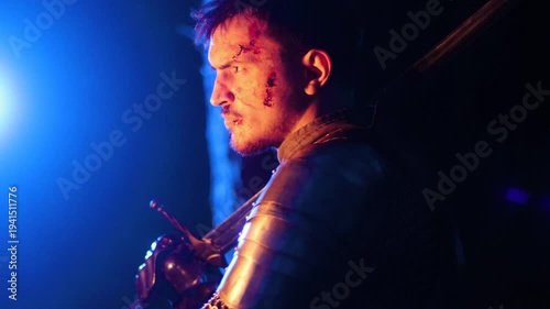 A knight in full armor, holding a sword and a torch, stands in a dark night forest. A medieval warrior with a bloodied face searches in the darkness.
