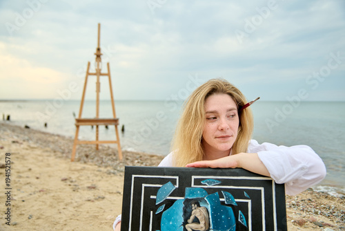 Fotografie Young female painter relaxing on beach with surrealist artwork in daylight