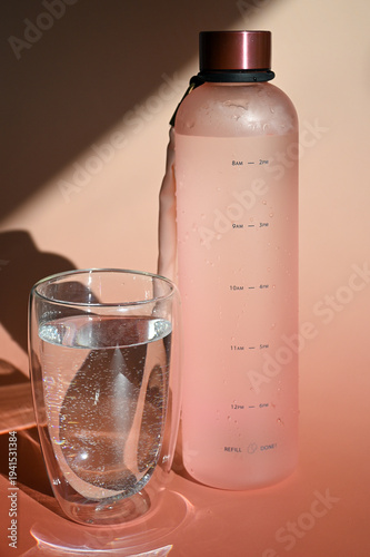 insulated water bottle and glass on sunlit peach surface promoting hydration and wellness