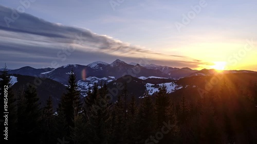 Timelapse of colorful sunset over winter mountain peaks with silhouettes of forest trees