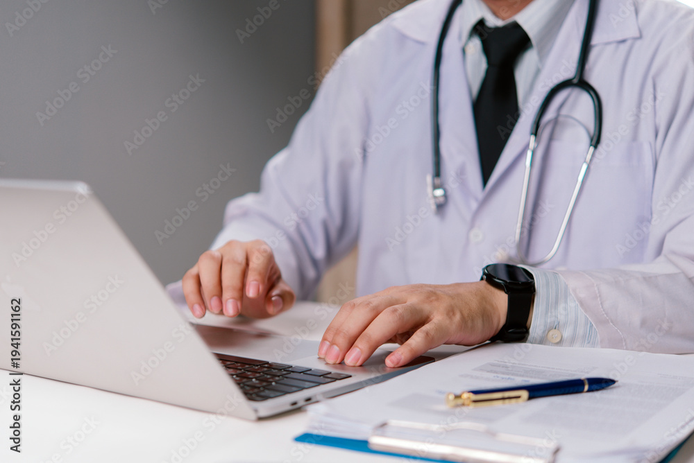 Fototapeta premium Doctor hands typing on laptop keyboard at hospital desk. Medical professional working on electronic health record data. Telemedicine and digital healthcare conce