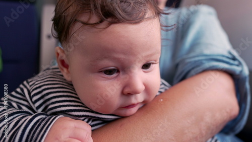 Konstfotografi Baby gazing up in mother’s arms on train, close-up of innocent expression, wide-