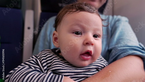 Fotografie Baby gazing up in mother’s arms on train, close-up of innocent expression, wide-