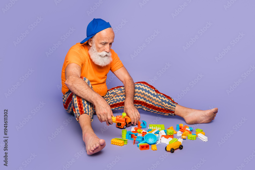 Obraz premium Carefree elderly man plays with colorful blocks on a purple background, wearing orange shirt and striped pants