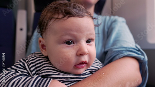 Fotografie Baby gazing up in mother’s arms on train, close-up of innocent expression, wide-