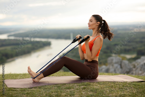 Принти на полотні Athletic young woman exercising with resistance bands on yoga mat atop scenic hi