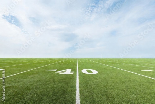 Wide-angle view of green football field at 40-yard line with white markings, blue sky background