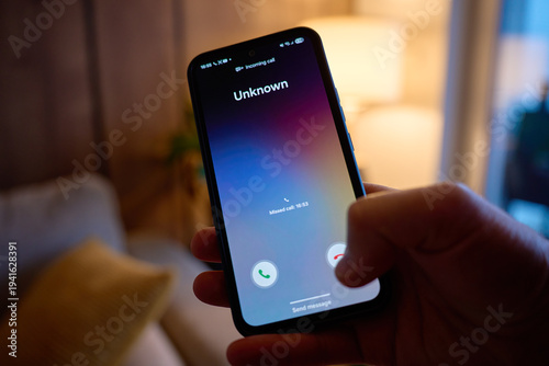 Fotografia Close-up of hand holding smartphone showing unknown incoming call in living room
