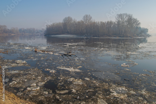 Obraz na płótnie A river with ice floes, bare trees on the banks under a clear blue sky