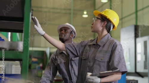 Diverse industrial workers checking metal part and inventory details on clipboard in warehouse factory