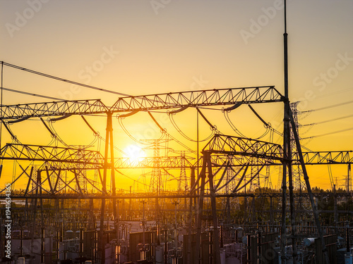 Silhouette of high voltage electrical substation and power transmission lines under a golden sunset sky for energy industry concept.