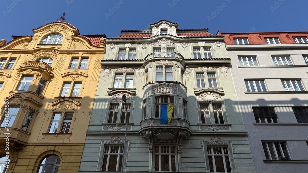 Fototapeta premium Old buildings stand side by side on a street in Prague with clear blue skies above during the day