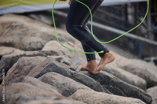Close-up of a surfer’s ankle secured with a safety leash while stepping toward the ocean, capturing the anticipation of entering the waves. The image highlights the connection between surfer and board