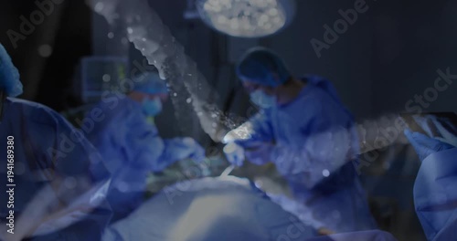 Medical team performing surgery under overhead surgical light, showing animated tablet data overlay