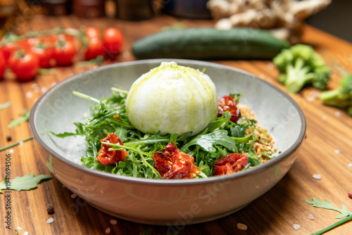 Gourmet burrata salad served in a rustic gray bowl. The creamy burrata sits on a bed of fresh arugula, topped with a drizzle of olive oil.