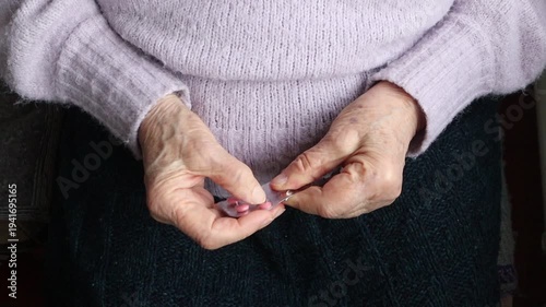 The hands of an elderly woman taking a pink pill out of a blister pack.