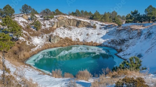 A tranquil winter landscape featuring a teal lake partly frozen, encircled by snowy banks & pines