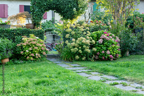Slika na platnu Lush garden entrance with ivy arch and blooming hydrangeas
