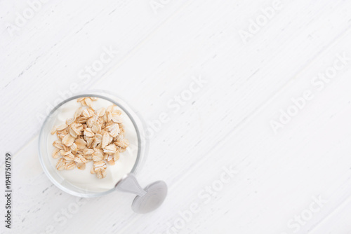 Greek yogurt with oatmeal in glasses with spoon over white wooden background with copy space