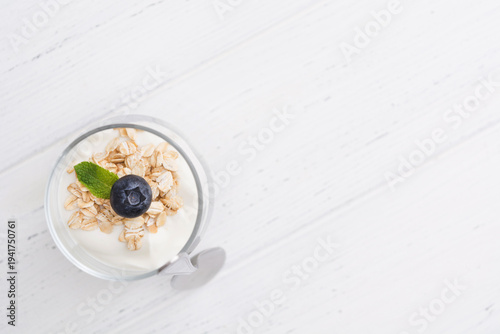 Greek yogurt with oatmeal and blueberry in glasses with spoon over white wooden background with copy space
