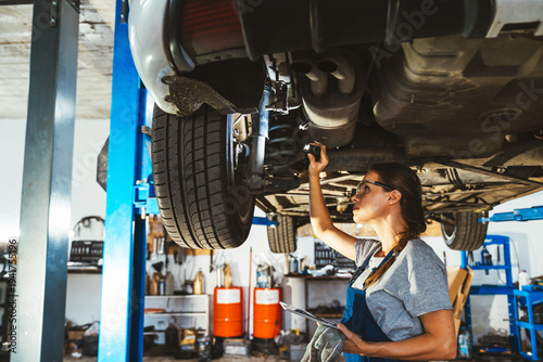 Young adult female mechanic inspecting car in auto repair shop